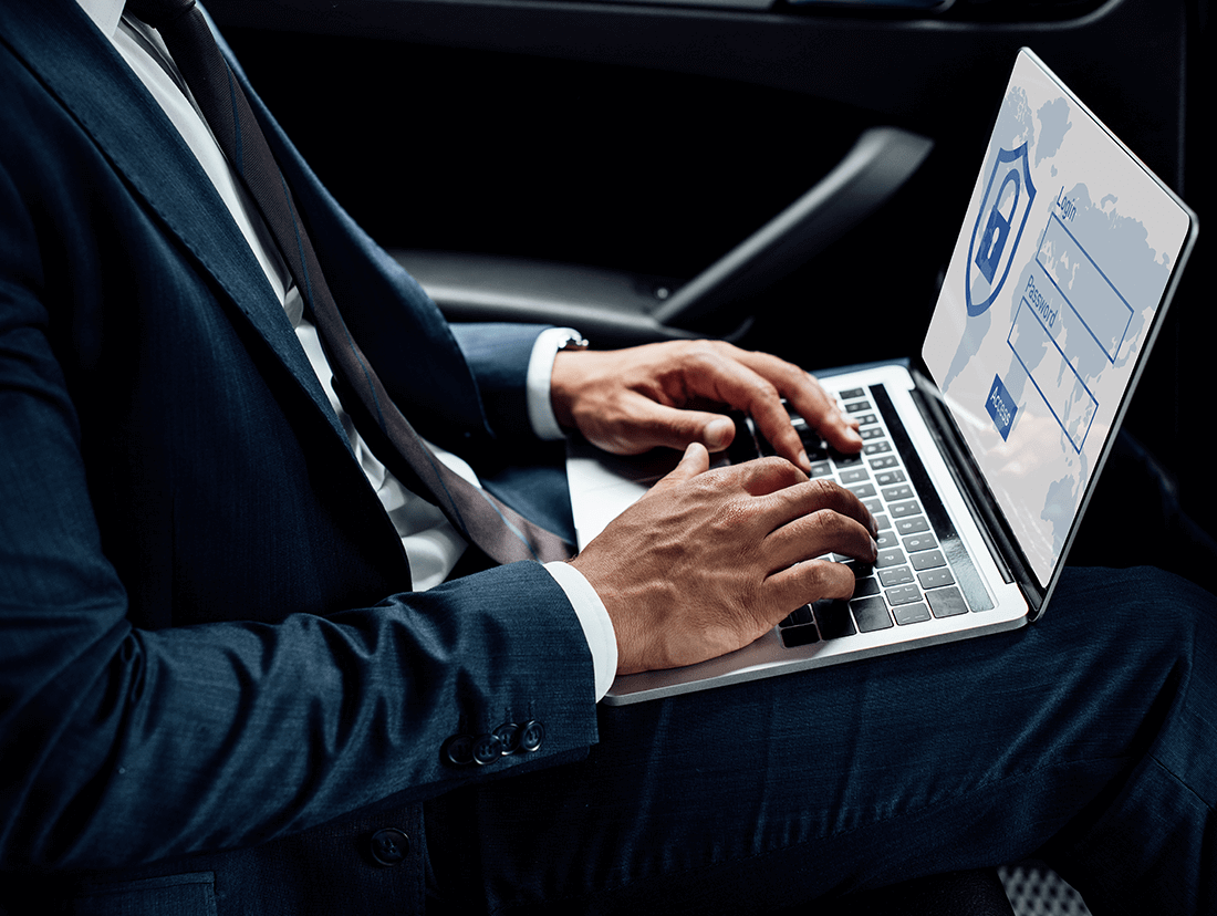 A man in a suit typing on a laptop in a car.